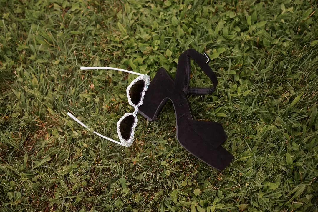 Wedding detail: black heeled sandals and decorated sunglasses left in the grass