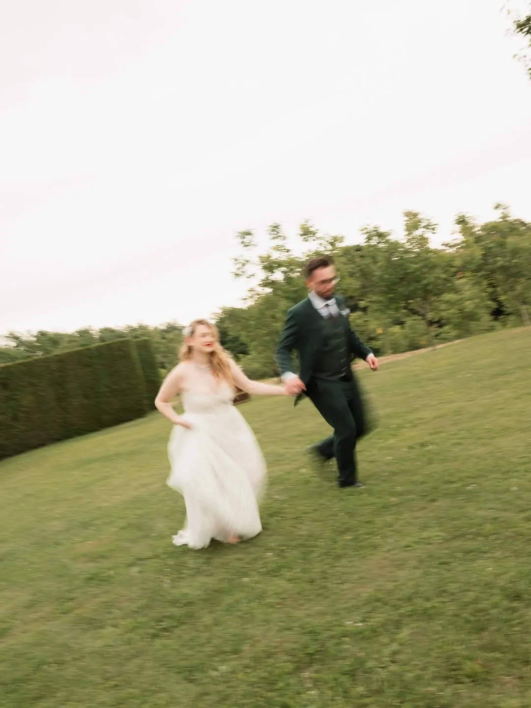 The couple hold hands and run across a lawn, shot with deliberate motion blur