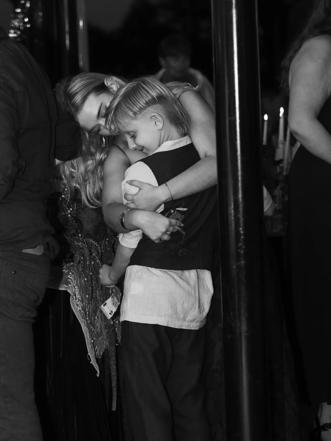 The bride in a lace dress hugs a young boy during the evening party, lit by candles