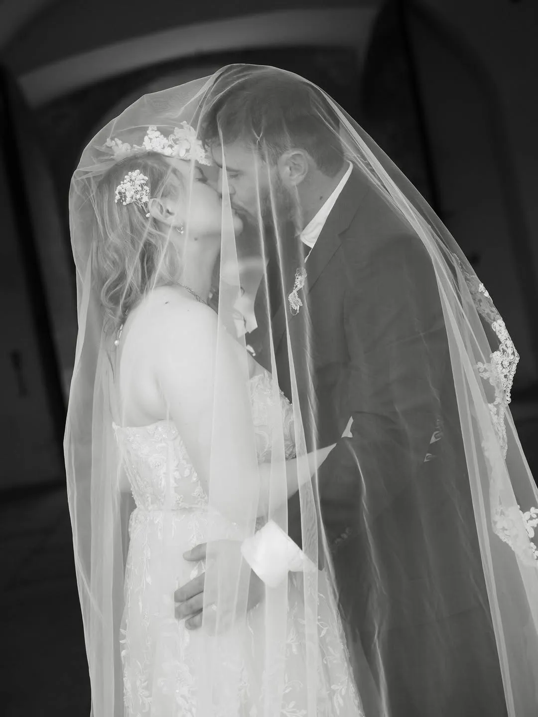 The couple kiss under a long lace veil that covers them both